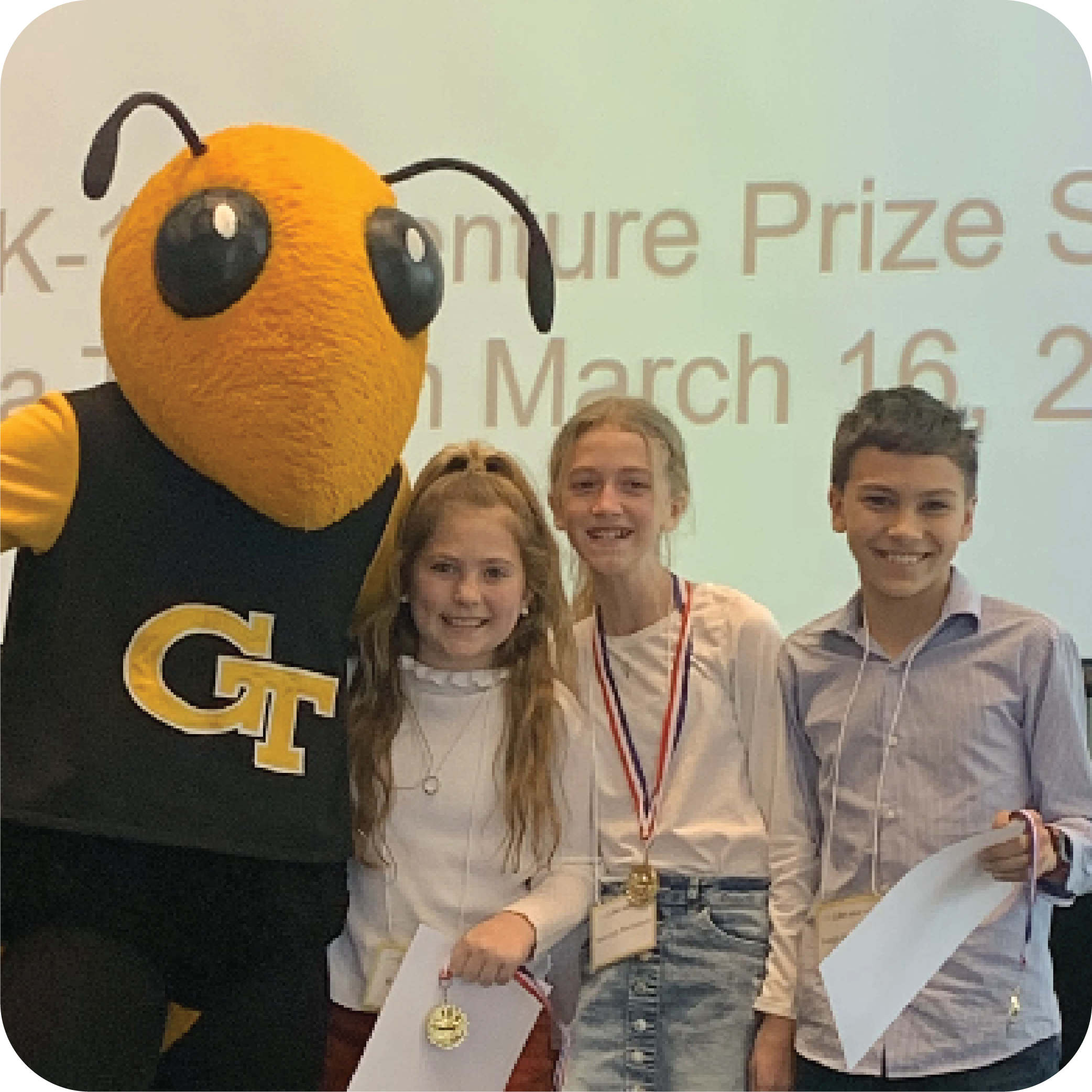 Three smiling students holding certificates and standing next to Buzz (Georgia Tech's yellowjacket mascot).